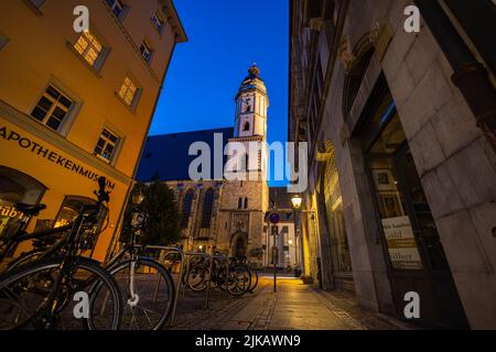 Leipzig, Deutschland - 02. Juli 2022: Thomaskirche oder Thomaskirche, Blick entlang der Burgstraße in einer Sommernacht. Gebäude, die von alten Straßenlaterden beleuchtet werden Stockfoto