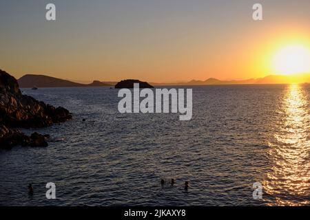 Touristen schwimmen bei Sonnenuntergang auf der Insel Hydra in Griechenland im Sommer Stockfoto