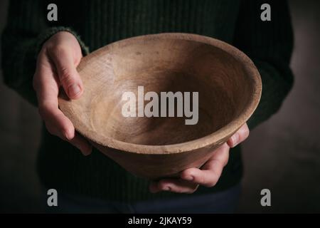Von oben der Ernte nicht erkennbar Weibchen in dunkler Abnutzung mit leeren runden Holzschale in den Händen Stockfoto