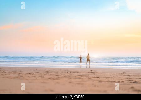 Ein Paar läuft am Strand. Ein glückliches Paar geht zum Sonnenuntergang ins Meer. Verschwommener Hintergrund für Sommerferien. Unverschämter Mann und Frau laufen auf dem Sandmeer Stockfoto