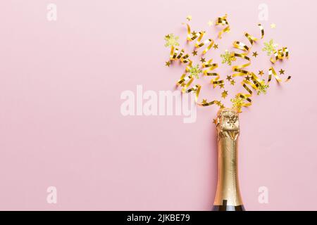 Kreative, flache Lay-Komposition mit einer Flasche Champagner und Platz für Text auf farbigem Hintergrund. Champagner-Flasche mit bunten Party-Streamer. Urlaub Stockfoto