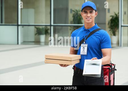 Fröhliche asiatische Lieferung Mann mit Pizza-Boxen geben Ihnen Tablet-Computer Stockfoto