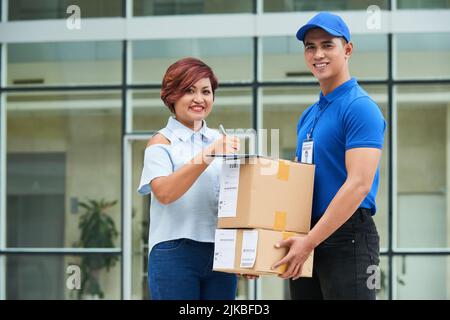 Fröhliche asiatische Frau Unterzeichnung Dokument beim Empfang von Paketen Stockfoto