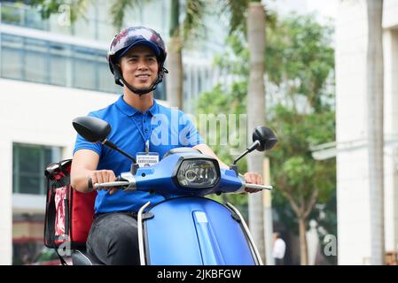 Vietnamesischer Lieferer im Helm, der auf einem Roller reitet Stockfoto