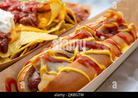 Street Food Hotdog in Ketchup und Senf mit Chili Nachos serviert Vorschlag erstickt. Stockfoto