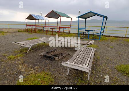 Alte Liegestühle und farbenfrohe Pavillons am Sevan-Ufer bei windigem Wetter Stockfoto