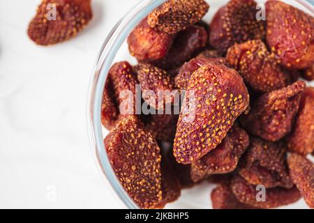 Nahaufnahme von getrockneten, dehydrierten Erdbeeren im Glasglas auf weißem Marmorboden. Sommerzubereitungen von Vitaminfutter für den Winter. Stockfoto