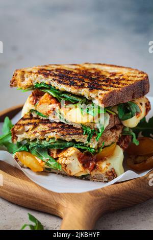 Gegrilltes Sandwich mit Gemüse und Mozzarella auf einem Holzbrett. Stockfoto