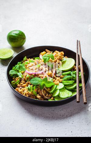 Thailändischer Hähnchensalat, Larb Gai mit Zwiebel, Gurke und Minze auf einem schwarzen Teller. Asiatisches Speisekonzept. Stockfoto