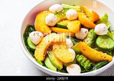 Sommer-Pfirsichsalat mit Avocado, Gurke und Mozzarella, Nahaufnahme. Gesundes Rezept, vegetarisches Lebensmittelkonzept. Stockfoto