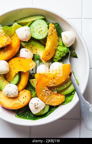 Sommer-Pfirsichsalat mit Avocado, Gurke und Mozzarella, Draufsicht. Gesundes Rezept, vegetarisches Lebensmittelkonzept. Stockfoto