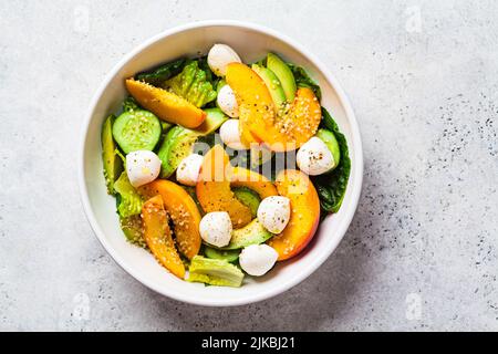 Sommer-Pfirsichsalat mit Avocado, Gurke und Mozzarella, Draufsicht. Gesundes Rezept, vegetarisches Lebensmittelkonzept. Stockfoto