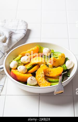 Sommer-Pfirsichsalat mit Avocado, Gurke und Mozzarella, Nahaufnahme. Gesundes Rezept, vegetarisches Lebensmittelkonzept. Stockfoto