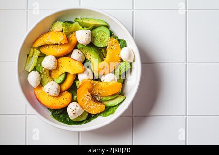 Sommer-Pfirsichsalat mit Avocado, Gurke und Mozzarella, Draufsicht. Gesundes Rezept, vegetarisches Lebensmittelkonzept. Stockfoto