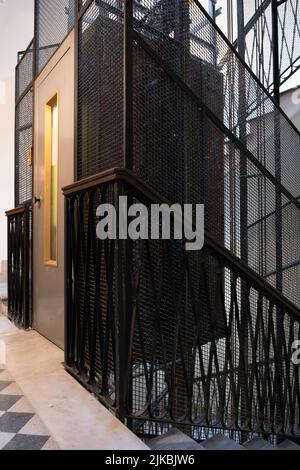 Treppenhaus mit Metallrahmen-Aufzugswelle, Drahtgeflecht-Käfig, Kabel und Kabine in einem alten Apartmentgebäude in Rom, Italien. Enge Schärfentiefe Stockfoto