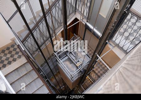 Dramatisch schoss ein älteres Aufzugsschachteln mit Metallrahmen, Zäunen, Kabeln und Aufzugstüren in einem alten Apartmentgebäude hoch. Enge Schärfentiefe Stockfoto