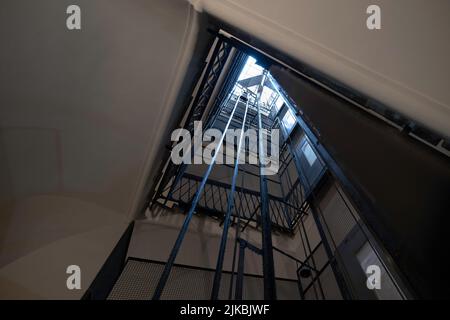 Dramatisch schoss ein älteres Aufzugsschachteln mit Metallrahmen, Zäunen, Kabeln und Aufzugstüren in einem alten Apartmentgebäude hoch. Enge Schärfentiefe Stockfoto