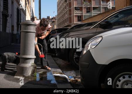 Frau füllt roten Trinkkrüg für ihren Hund mit frischem Trinkwasser aus einem antiken öffentlichen Trinkbrunnen namens „nasoni“ (große Nasen) in Rom Stockfoto
