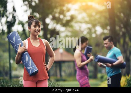 Ziemlich glückliche junge Yogi, die mit ihren Freunden im Park praktiziert Stockfoto