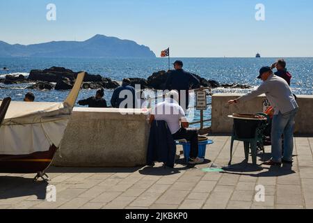 Fischer reparieren Fischernetze am Ufer des Küstendorfes mit dem Vorgebirge von Portofino im Hintergrund, Boccadasse, Genua Stockfoto