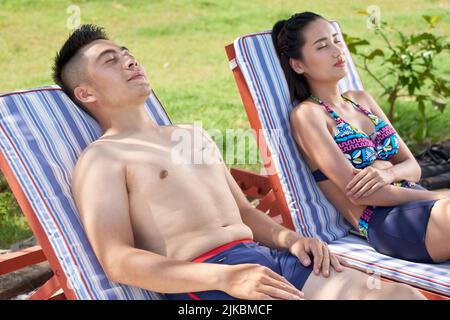 Schönes vietnamesisches junges Paar, das sich auf den Chaiselongue-Liegen entspannen kann Stockfoto