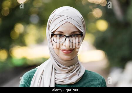 Porträt einer jungen muslimischen Frau, die im Stadtpark einen Hijab-Kopftuch trägt, während sie die Kamera anschaut. Nahaufnahme einer fröhlichen Frau, die mit einem Kopftuch im Freien lächelt. Casual islamischen Mädchen auf die Natur. Stockfoto