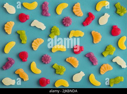 Gelee-Bonbons in Form von Früchten, Bäumen und Vögeln als Muster auf blauem Hintergrund Stockfoto