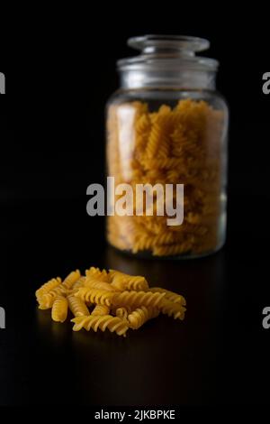 Fusilli-Pasta vor dem Glas auf schwarzem Hintergrund Stockfoto