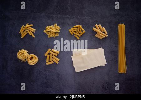 Verschiedene Arten von Nudeln, darunter Penne, Fusilli, Farfalle, Spaghetti, Lasagne, Tagliatelle, papiri, Tortiglioni zusammen auf einem Hintergrund Stockfoto