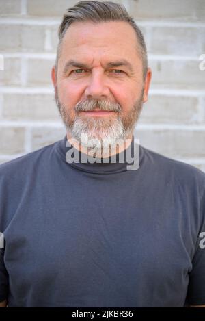 Ernsthafter Mann mittleren Alters, der in einem Nahaufnahme-Porträt nachdenklich auf die Kamera schaut Stockfoto