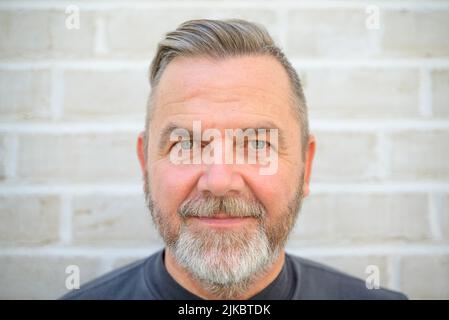 Bärtiger Mann mittleren Alters starrte in einem Nahaufnahme-Kopfschuss gegen eine Backsteinmauer aufmerksam auf die Kamera Stockfoto