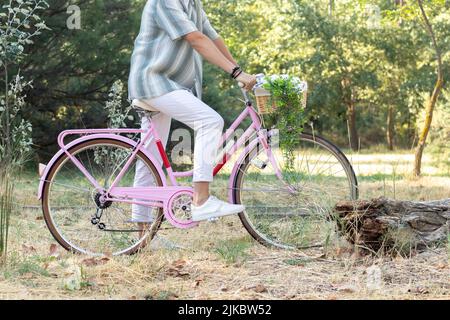 Seitenansicht eines nicht erkennbaren jungen Hipster-Mannes auf einem pinken Vintage-Fahrrad mit natürlicher Umgebung im Hintergrund Stockfoto