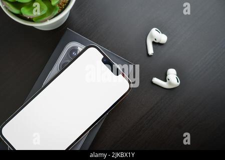 KIEW, UKRAINE - 10. FEBRUAR 2022: Ausgepackt neues Apple iPhone 13 Pro Space Grey mit leerer Seite und AirPods Pro Kopfhörern auf schwarzem Hintergrund. Stockfoto