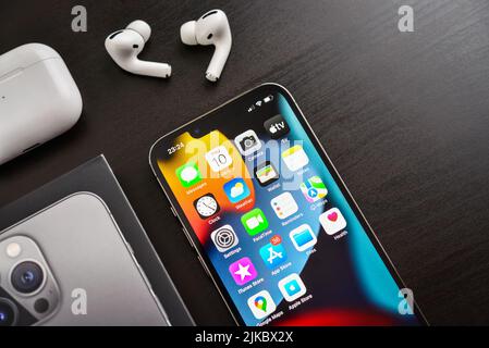 KIEW, UKRAINE - 10. FEBRUAR 2022: Ausgepacktes neues Apple iPhone 13 Pro Space Grey mit AirPods Pro Kopfhörern auf schwarzem Hintergrund. Stockfoto