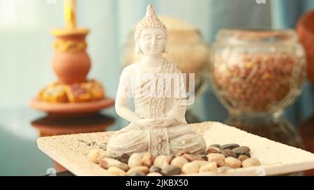 Nahaufnahme einer weißen Tischskulptur eines meditierenden Buddha auf einem Teller mit Steinen Stockfoto