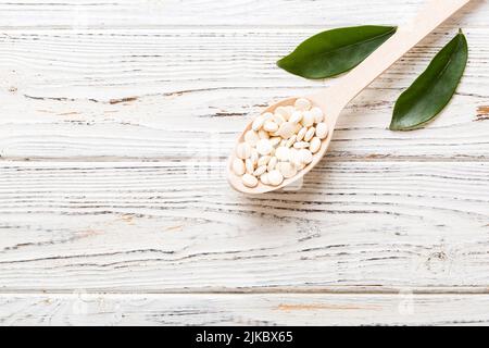 Haufen weißer Pillen auf farbigem Hintergrund. Tabletten auf einem Tisch verstreut. Haufen roter weicher Gelatinekapsel. Vitamine und Nahrungsergänzungsmittel Konzept. Stockfoto