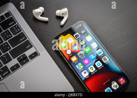 KIEW, UKRAINE - 10. FEBRUAR 2022: Apple-Produkt. MacBook Pro, iPhone 13 Pro mit AirPods Pro Kopfhörern auf schwarzem Hintergrund Draufsicht. Technologie-ga Stockfoto