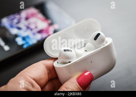 KIEW, UKRAINE - 10. FEBRUAR 2022: Ladetasche mit AirPods Pro Kopfhörern und dem neuen iPhone 13 Pro mit Apple Music App auf dem Bildschirm Stockfoto