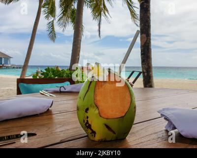 Grüne tropische Kokosnuss auf dem Tisch vor dem Hintergrund eines wunderschönen Strandes und Palmen Stockfoto