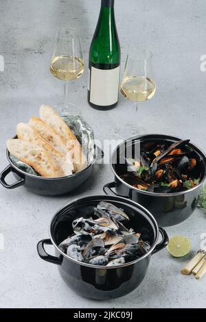 Töpfe mit Austern, gekocht und frittiert. Daneben ein Glas Wein Stockfoto