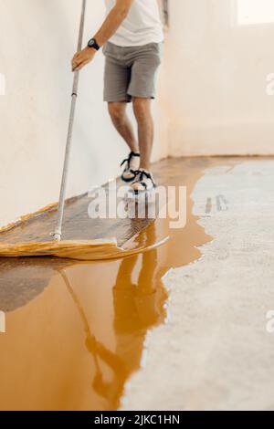 Nahaufnahme eines Handwerkers, der gelbe flüssige Farbe auf einen neuen Boden aufgetragen hat Stockfoto