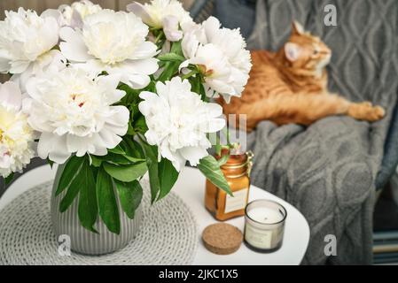 Blumenstrauß aus weißen Pfingstrosen auf dem Couchtisch mit Kerzen im Innenraum Stockfoto