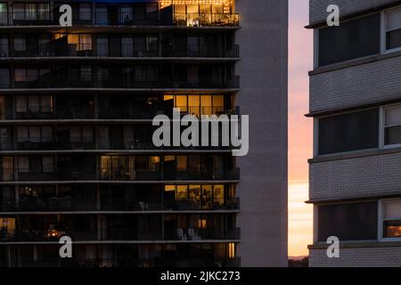 Sonnenuntergang hinter zwei Gebäuden. Dekorierte Glühbirnen funktionieren auf einem Balkon im obersten Stock. Stadtleben Konzept. Stockfoto