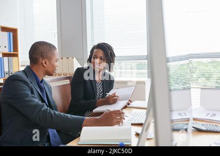 Die hübsche afroamerikanische Managerin und ihre junge Kollegin versammelten sich in einem modernen Sitzungssaal und diskutierten produktiv über ihr gemeinsames Projekt Stockfoto