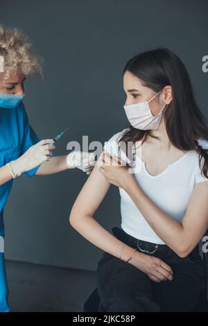 Ärztin in Schutzmaske zur Vorbereitung auf die Injektion eines Impfstoffs gegen Coronavirus in den Arm des Patienten. Medizinisches Gesundheitskonzept. Coronavirus Stockfoto