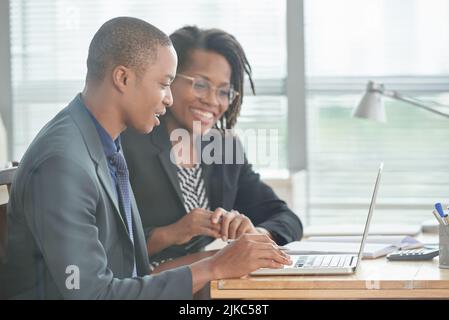 Fröhliches Team von Finanzmanagern in formalwear, die am Schreibtisch sitzen und Jahresabschlüsse mit Hilfe eines Laptops vorbereiten, Inneneinrichtung des Großraumbüros im Hintergrund Stockfoto