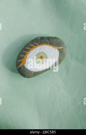Gold, weiß, mintgrün bemalter böser Augenrock auf grünem Leder Stockfoto
