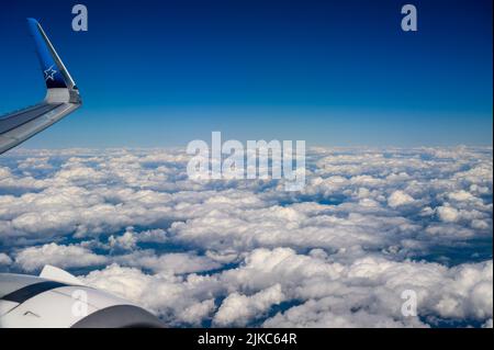 Über den Wolken: Die Flügelspitze und der Düsentoolmotor eines Air Transat Airbus A321, der über weißen Cumuluswolken über der Südküste Englands fliegt. Stockfoto