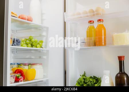 Vorderansicht der offenen, zweitürigen Kühl- oder Kühlschranktür, gefüllt mit frischem Obst und Gemüse, voll mit gesunden Lebensmitteln und Zutaten im Inneren. Elektrische Küche und Haushaltsgeräte Stockfoto