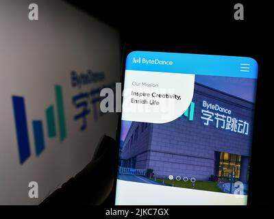 Person, die Mobiltelefon mit der Website des chinesischen Technologieunternehmens Bytedance Ltd. Auf dem Bildschirm vor dem Logo hält. Konzentrieren Sie sich auf die Mitte des Telefondisplays. Stockfoto